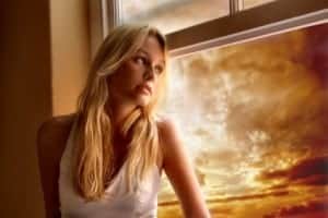 A beautiful woman gets a portrait photo taken of her while sitting in a window sill and looking out.