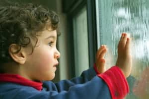 Portrait photo of a boy looking out through a window at a rain storm.